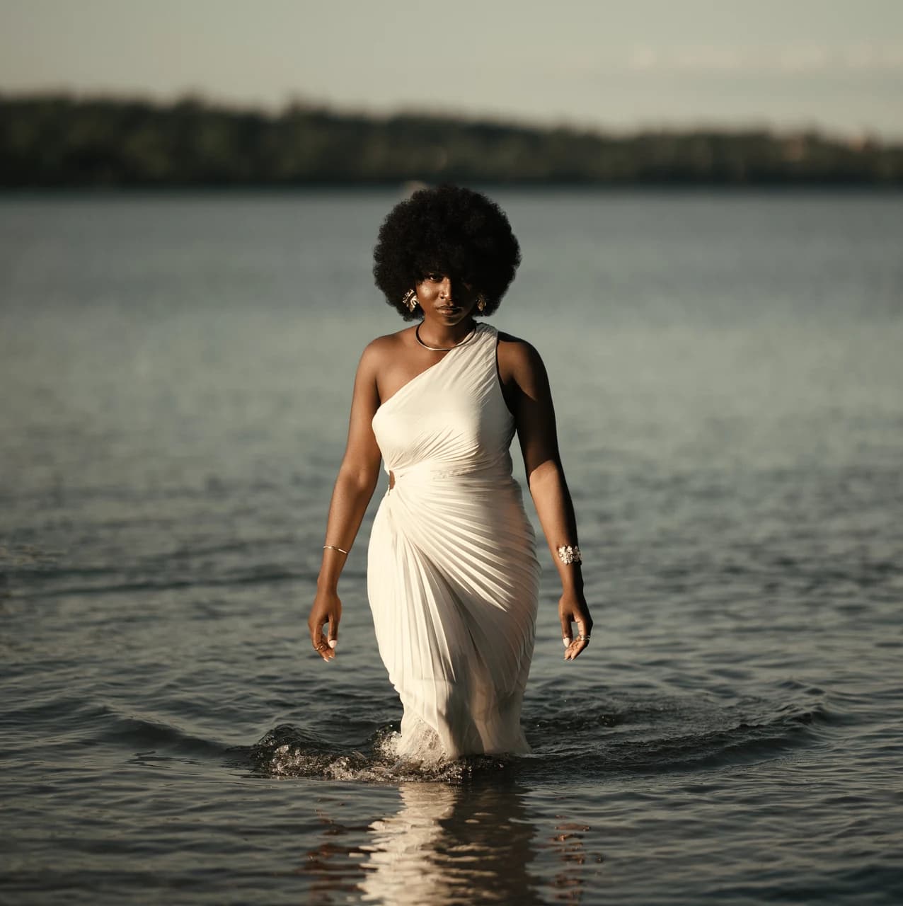 Woman in a white one-shoulder dress walking through a lake at dusk, edited with the Cinematic presets