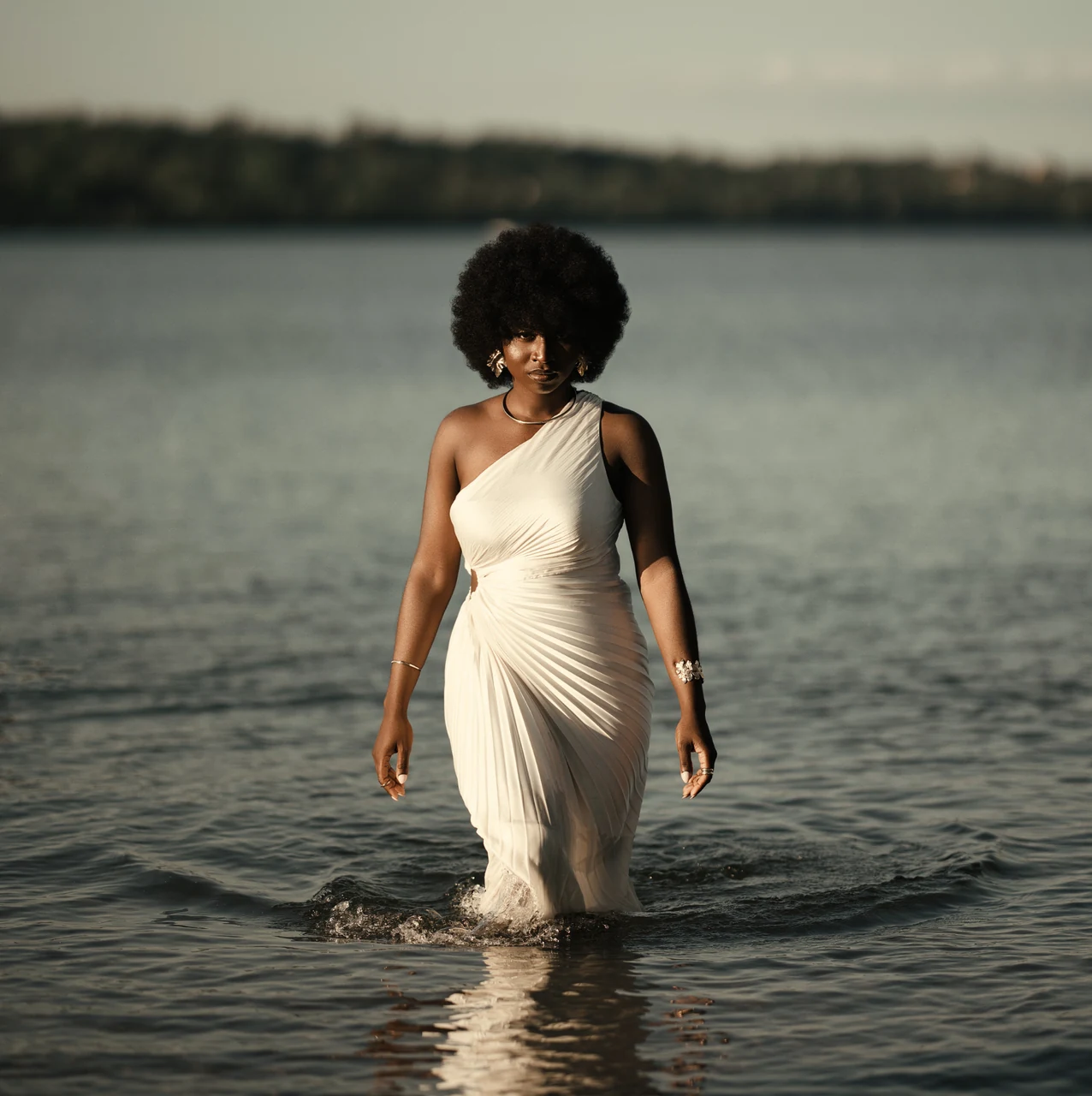 Woman in a white one-shoulder dress walking through a lake at dusk, edited with the Cinematic presets